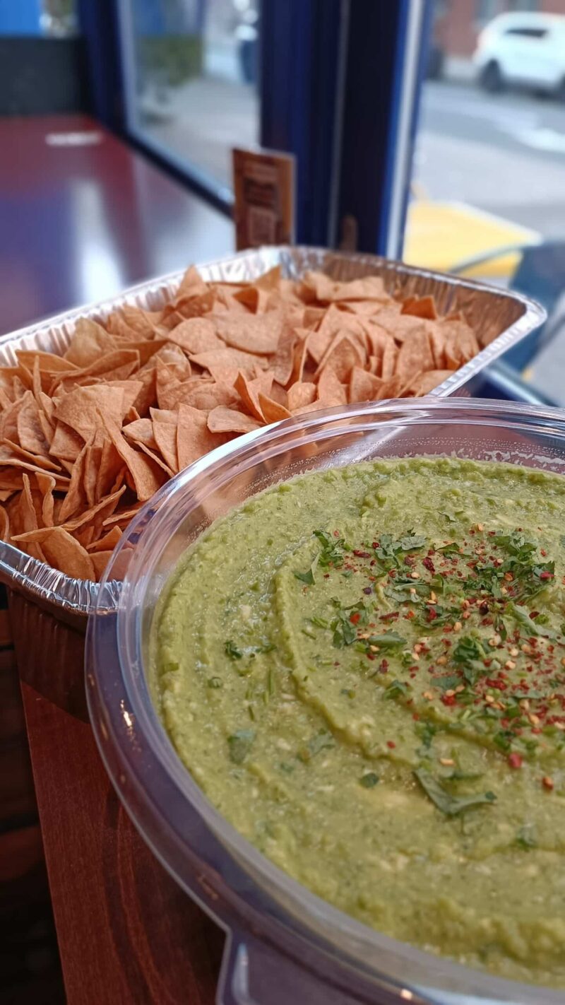 A bowl of guacamole with a tray of house made tortilla chips on a wooden table. Perfect for parties or as an appetizer.