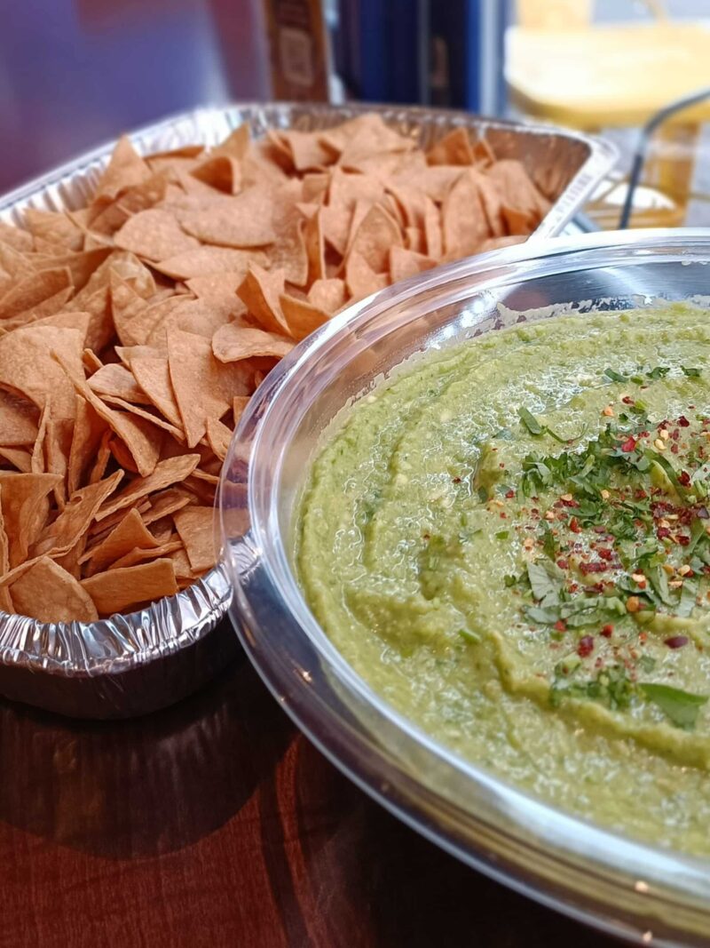 A bowl of guacamole with tortilla chips on a wooden table. Perfect for snacking or as an appetizer.