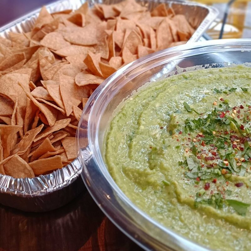 A bowl of guacamole with tortilla chips on a wooden table. Perfect for snacking or as an appetizer.