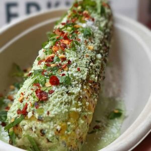 A tray featuring El Merkury's street corn elote loco, adorned with flavorful toppings for a delightful treat.