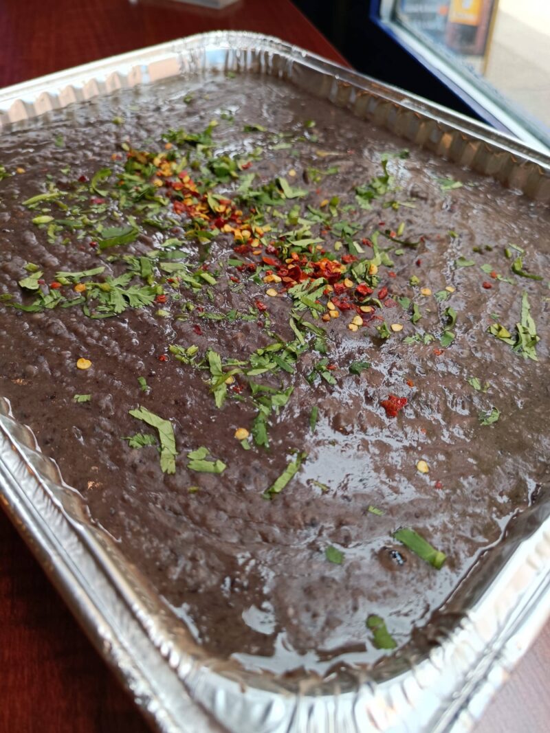 Tray of refried beans, featuring pinto Black bean mix, blended with garlic, jalapeno and spices.