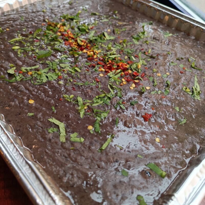 Tray of refried beans, featuring pinto Black bean mix, blended with garlic, jalapeno and spices.